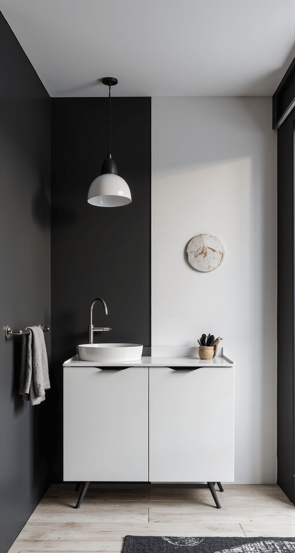 Strakke, monochrome babykamer met matte zwarte kledingkast, wit ledikant met zwart frame, geometrische messing mobile en zwart-wit tapijt. Diagonaal camerastandpunt laat industriële spots en lichtinval door jaloezieën zien.