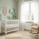Lichte Scandinavische kinderkamer met witte wieg tegen een zacht saliegroene muur, natuurlijke rieten schommelstoel en minimalistieke witte commode, verlicht door ochtendlicht dat door sheer linnen gordijnen valt.