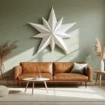 Een Scandinavische woonkamer met een grote witte papieren sterdecoratie van 90 cm, gemonteerd op een salie groene muur, met ochtendzonlicht dat door hoge ramen stroomt, een vintage cognackleurige leren bank, berkenhouten bijzettafels, een crème-kleurig vloerkleed, minimalistische styling en textuur op de muren.