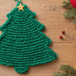 Close-up van een half voltooide gehaakte kerstboom in smaragdgroen garen op een eiken houten tafel, omringd door kleurrijke wolbollen en glanzende haaknaalden, met een vintage schaar en antieke stopnaalden in een rieten mandje, verlicht door natuurlijk ochtendlicht voor een warme Scandinavische sfeer.