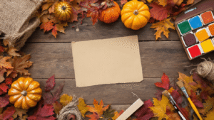 Bovenaanzicht van een warme herfst DIY werkruimte met een rustieke houten tafel, omringd door kleurrijke gedroogde bladeren, metallic geschilderde pompoenen, en diverse creatieve materialen zoals acrylverf, penselen, en jutedraad.