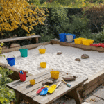 Zonnige tuin met houten zandbak, kleurrijke emmers en scheppen, beschilderde stenen op een picknicktafel, herfstbladeren en riverstenen op een plank, een geheime hut van takken, vintage kookgerei en een kind in een schort die speelt.