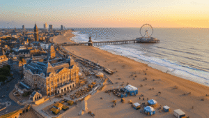 Scheveningen Strand: De Ultieme Nederlandse Kustbestemming Die Je Niet Wilt Missen! Aerial view of Scheveningen beach at sunset, featuring the golden sand coastline, Kurhaus Hotel, 382-meter pier with Ferris wheel, lighthouse, bustling Noorderstrand with beach clubs, peaceful Zuiderstrand, and colorful beach pavilions, with The Hague skyline in the background.