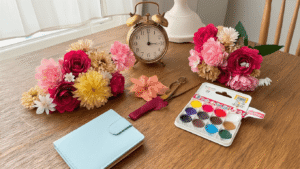 Knutselen met Geld: Slimme DIY-projecten die je Portemonnee Blij Maken Gezellige knutselhoek met kleurrijke crêpepapier bloemen, satijnen lint rozen en kartonnen portemonnee onderdelen, verlicht door warm gouden licht, met vintage houten tafel vol knutselmaterialen.